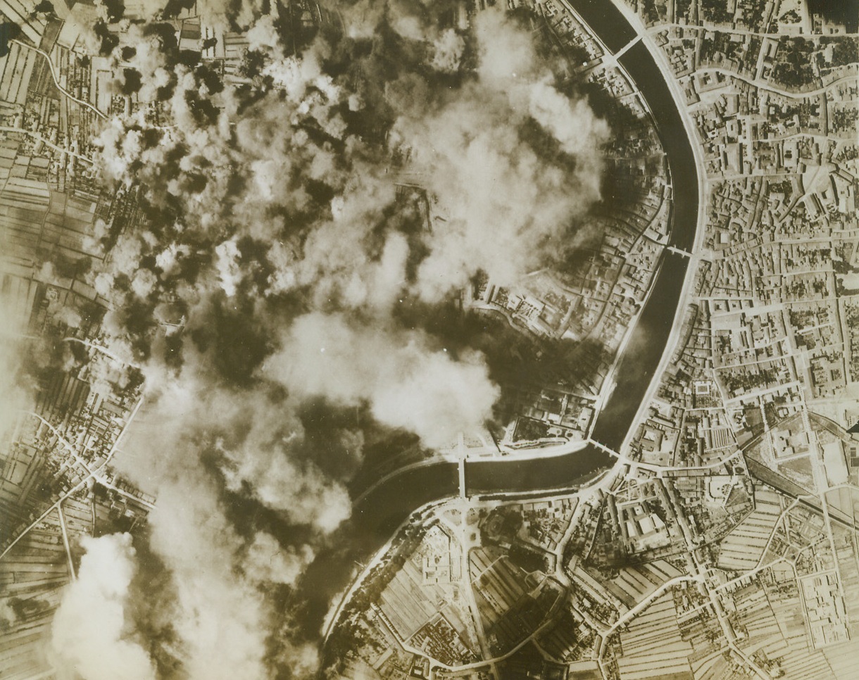 Two More Military Targets Picked Off, 9/12/1943. Italy – A double-track electrified railroad and the Piaggio Aircraft Factory in Pisa, Italy, get a load of bombs from U.S. Flying Fortresses. The River shown is the Arno, and the road and bridge at lower left of photo lead to the famous Leaning Tower of Pisa which was not disturbed. Credit: Army Air Forces photo from ACME;