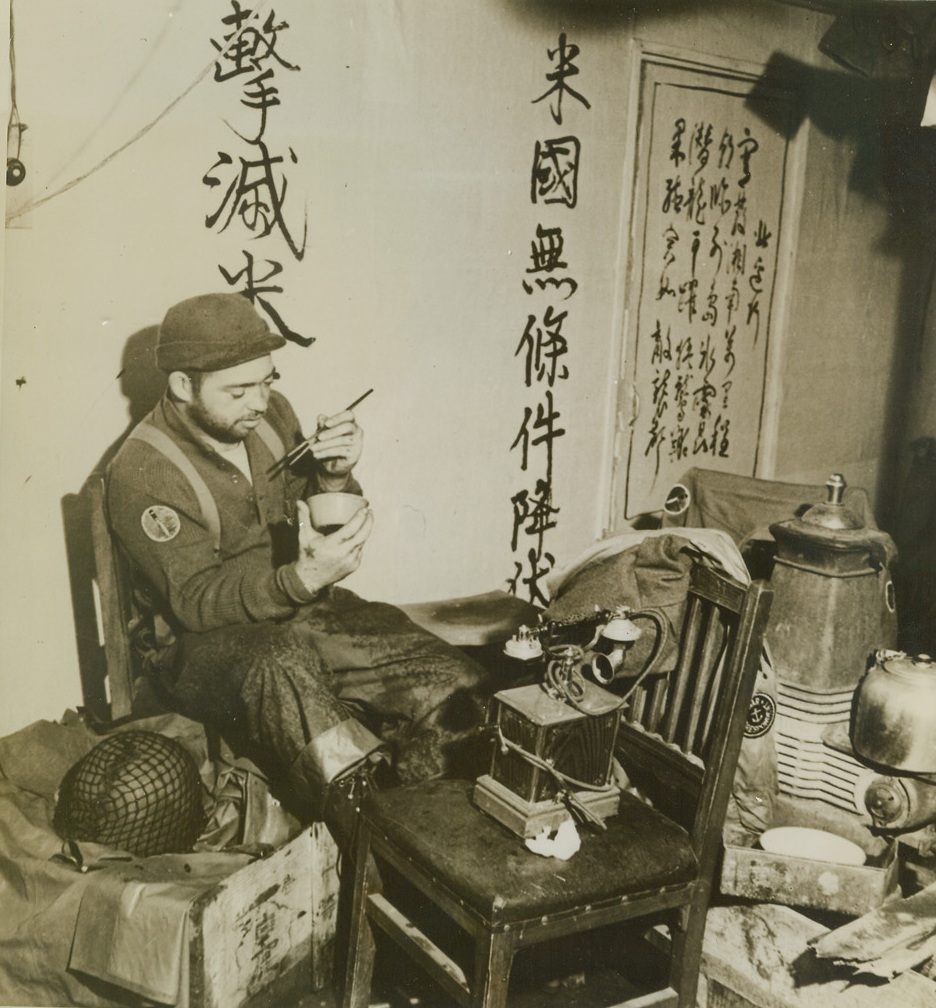 The Rice They Left Behind, 9/4/1943. Kiska --  The rice left behind when the Japs fled the island of Kiska makes a tasty titbit for S/Sgt. Edmond A. Birdsell of San Francisco, Calif.  Sitting in a shed cluttered with all kinds of equipment, the Yank samples the oriental food, using the enemy’s chopsticks. Credit line –WP—(ACME);