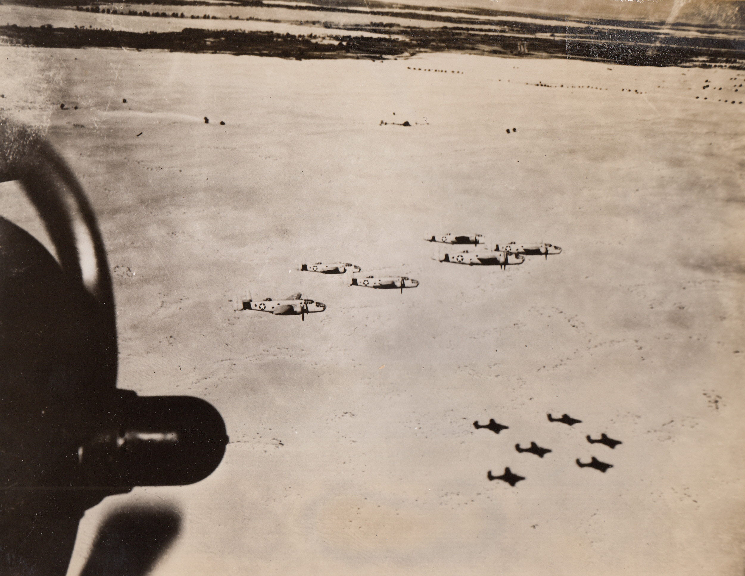American Planes Over African Desert, 9/12/1943. Middle East – Medium bombers of the U.S. Army Air Force fly in formation over the bleak desert in the Middle East, where they are harrying the supply lines and bases of the axis.  The planes are camouflaged so as to blend with the color of the desert, but there is no way of erasing the sharp shadows.;