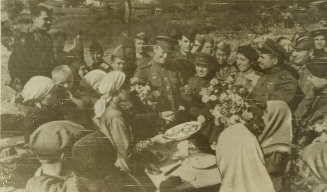 Freed From the Nazi Yoke, 9/19/1943. Bryansk, Russia—Soviet fighters who helped drive the Germans from Bryansk are treated to food and flowers by overjoyed Russian women who have been under the rule of the Nazis since October, 1941. The fall of the strong hedgehog defense of the German line was one of the most spectacular triumphs of the German defensive. Credit: ACME radiophoto.;