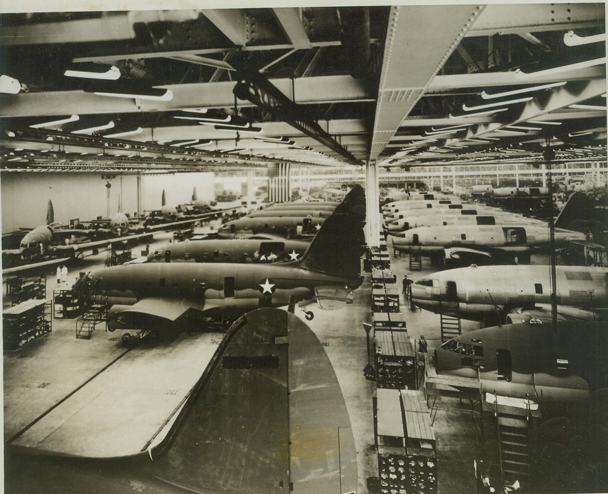 Mass Production For Air Giants, 10/15/1943. Buffalo, N.Y. – The giant Curtiss (C-46) Commando, largest twin-engine cargo aircraft type in the world, will go into mass production on the largest scale ever projected in peace or in war or a transport plane. This photo, taken in one of the two Buffalo plants of Curtiss-Wright Corporation, show the huge twin-engined cargo planes in various stages. When the aircraft in the line at right reach a certain stage in construction, they are transferred to the center line, and finally to the line at the left where they are completed.  Credit: (ACME);