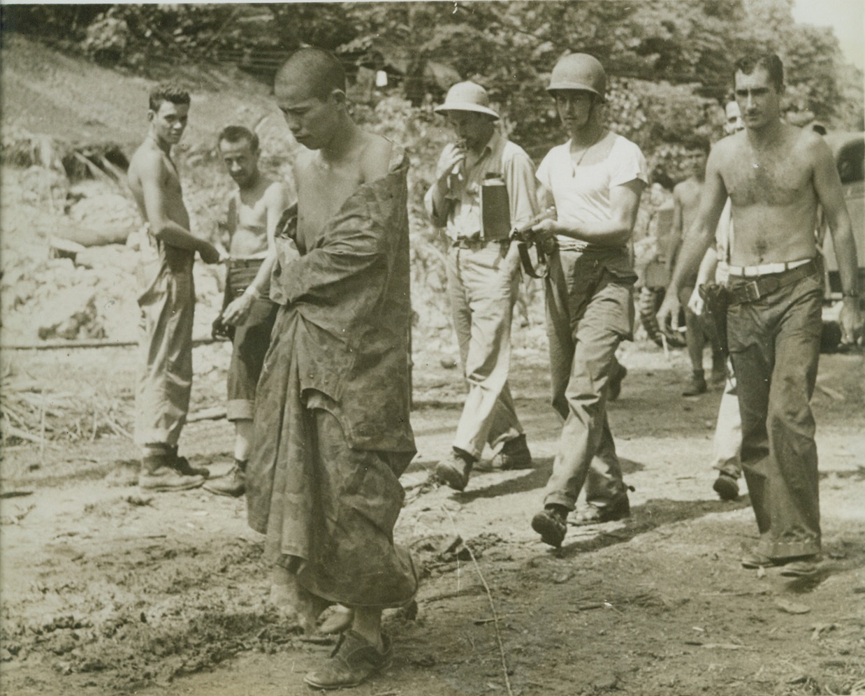 CAUGHT WITH HIS PANTS DOWN, 10/30/1943.  SOMEWHERE IN THE SOUTH PACIFIC – This Jap pilot was fished out of the ocean sans clothing, after he was shot down by an American PT boat. The torpedo craft’s skipper loaned him this poncho which he wears as he is ushered to U.S. Navy Headquarters by some tough U.S. fighters. Credit: OWI Radiophoto from ACME;