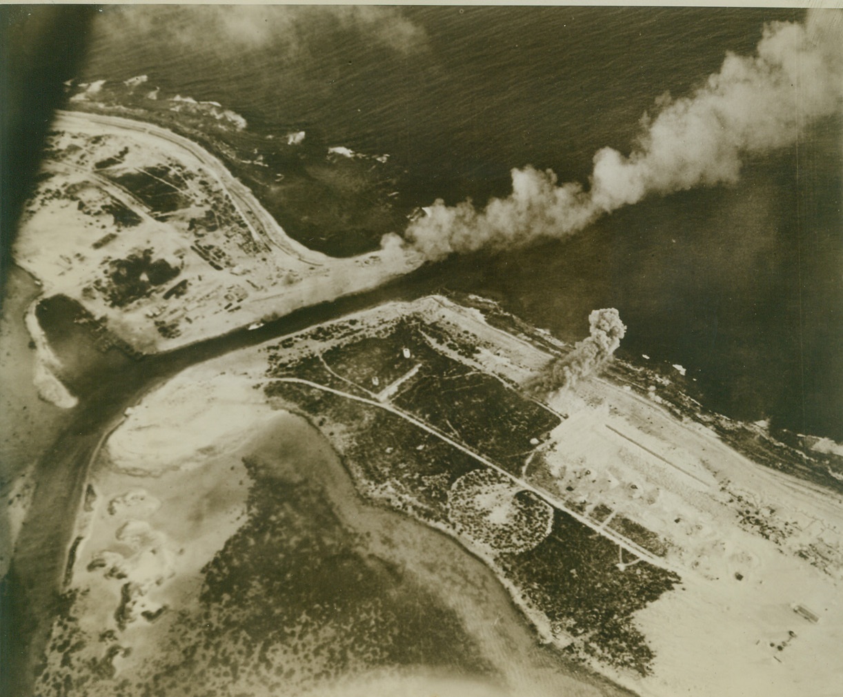 TANKER BURNS AS WAKE IS RAIDED, 10/13/1943. A small Jap tanker burns in the channel between enemy-held Wake Island (Left) and Wilkes Island (Right) as bombers of the U.S. Navy Task Force that raided the 3-island Wake Group pass over. Storage tanks have just been hit near the coast of Wilkes. Three hundred and twenty tons of bombs fell on Wake during the 2-day raid. Credit: U.S. Navy photo via OWI Radiophoto from ACME;