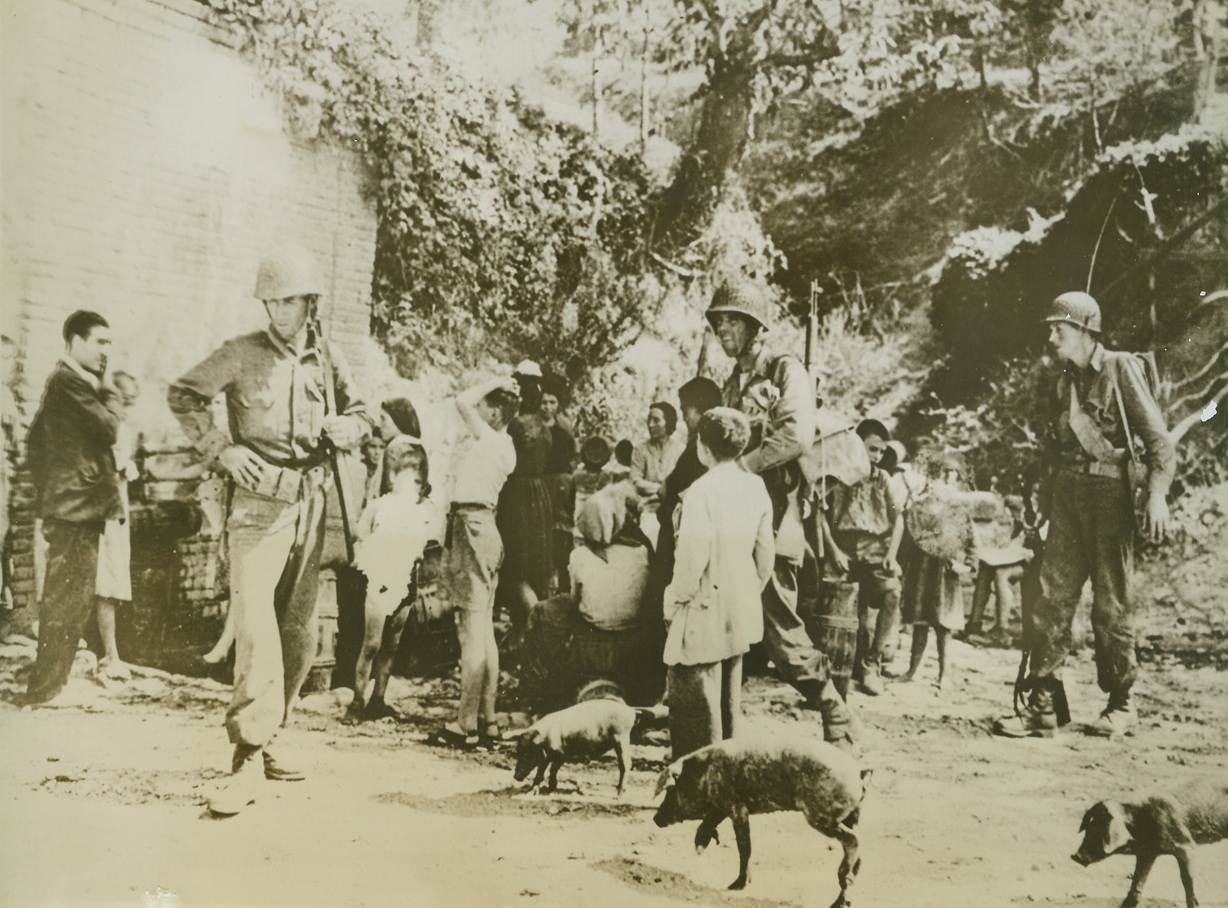 Pigs In The Streets, 10/14/1943. ALTAVILLA, ITALY—Walking through the streets of liberated Altavilla, Fifth army warriors have to be careful not to trip over porkers that wander about.  Coming out of hiding after allied troops took the town, liberated Italians gather in background to read posters put up by the allied military government. Credit:  ACME;