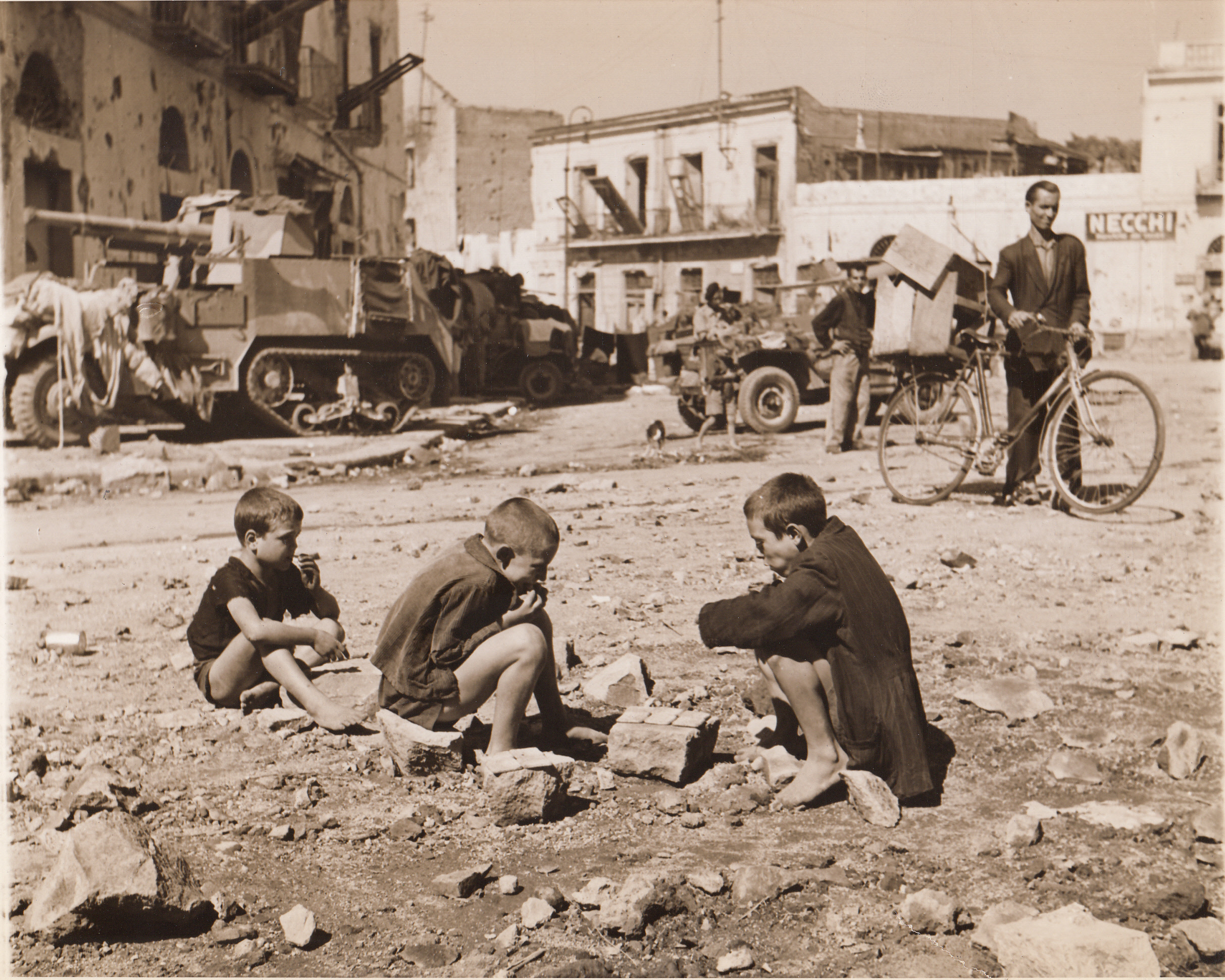 Hunger Appeased, 10/11/1943. ITALY—A far cry from an American outdoor picnic is this little group of Italian youngsters who cram biscuits in their mouths in the center of a war-torn street of Torre Annunziata. The barefoot kids huddle over the food, probably the first substantial bite they have had in a long time.;