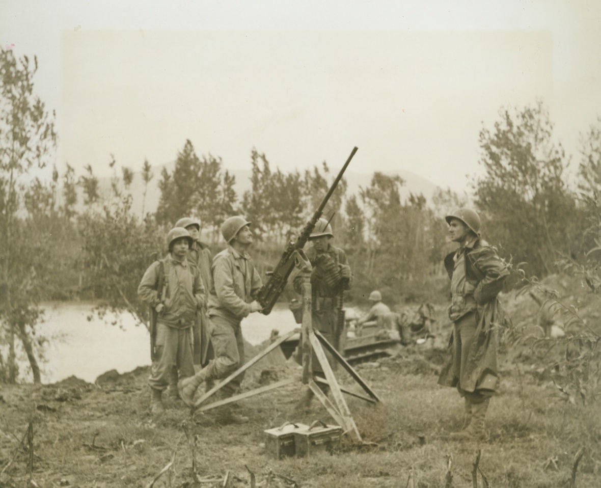 NAZI HOPES DROWNED IN THE VOLTURNO, 10/25/1943. . William George, Rensselaer, Ind. (behind gun); ITALY—When 5th Army troops splashed, paddled or swam across the Volturno, more than a river was lost to the Germans. The Nazis learned in blood that their natural barrier defense system wouldn’t work. To further consolidate this message of Axis defeat, crack American engineers immediately floated a pontoon bridge across the shallow river so that heavy Allied equipment could rumble on the heels of the advanced infantry forces who had begun the job of dislodging the enemy. These photos tell the story of that bridge which, in reality, may be called a road to victory in Italy for the Allies.  NEW YORK BUREAU An anti-aircraft gun crew guards against enemy raiders as bulldozers (background) break ground for the bridge approach. Members of the gun crew are (left to right): Pvt. Manuel Ortga, Beeville, Tex., Sgt. John Tomalesky, Cleveland, Ohio; Pvt. James Mize, Reading, Ohio, holding ammunition, and Lt. James Bowman of St. Louis, Mo. Credit: Acme photo by Bert Brandt, War Pool Correspondent;