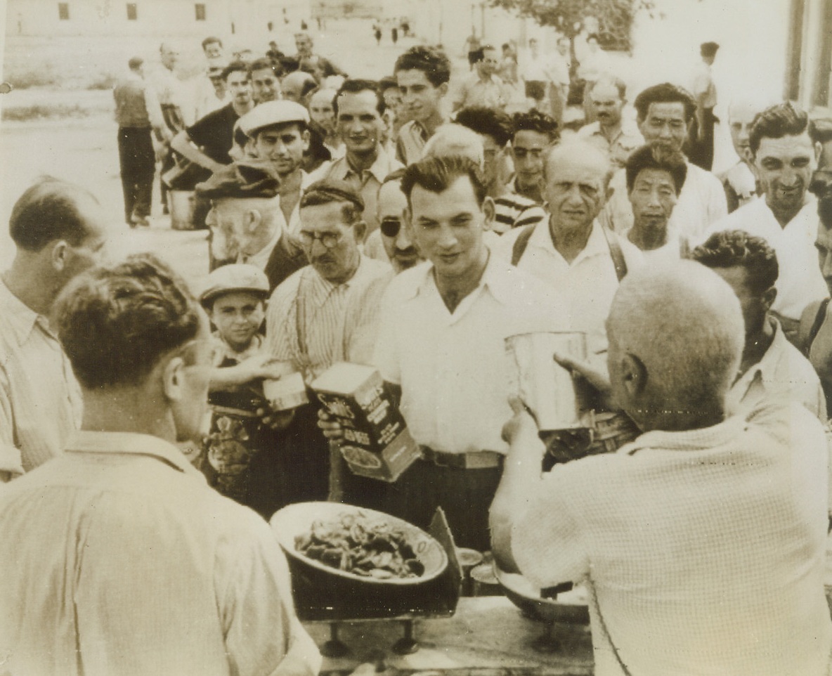INTERNEES GET AMERICAN FOOD, 10/2/1943. ITALY—Over 1500 German Jews, Poles, Yugoslavs, French, Czechs and a few Chinese were held in barbed wire enclosures at a huge concentration camp near St. Di Barraccano until freed by Allied liberators. Here the internees are issued rations (note American labels) by British 8th Army personnel. Though the internees are freed, they as yet have no homeland to which they can return. Photo radioed tonight to New York. Credit: OWI radiophoto from Acme;