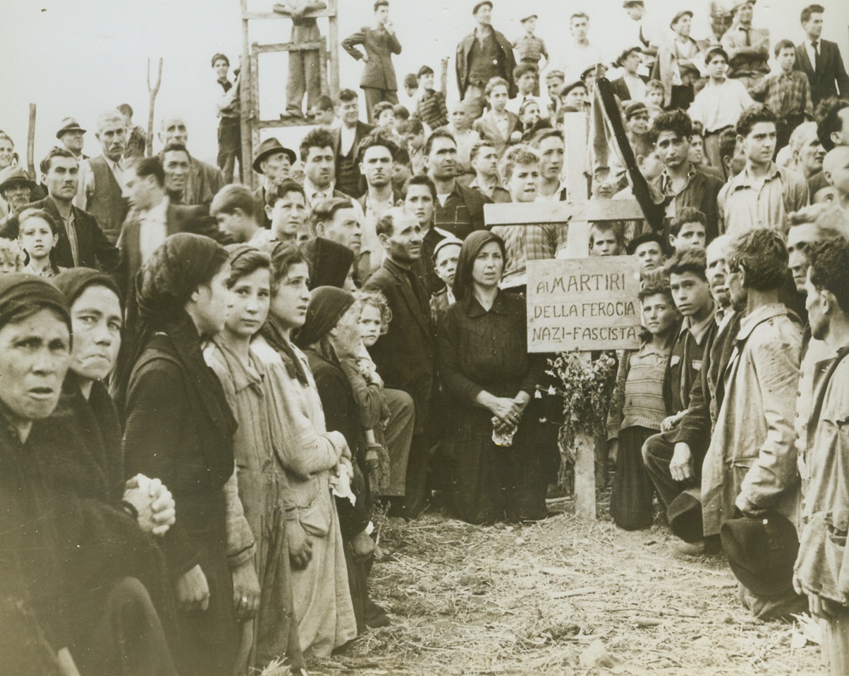 Bury Victims of Nazi Mass Murder, 10/29/1943. ITALY – A Canadian Army photographer took this picture of the wives and families of 16 Italians massacred by Germans at Rionero. This mass killing was the Nazi answer to the shooting of a German chicken thief by an Italian. Inscription on cross says men were martyrs of Nazi and Fascist ferocity. Credit Line (ACME);