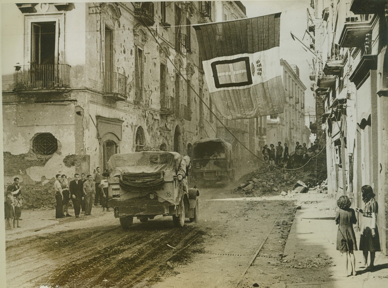 Welcome to Resina, 10/14/1943. RESINA, ITALY -- Residents of Resina gather in the streets and climb atop bomb-debris on the sidewalk to watch vehicles of the Allied Fifth Army enter their town. Shattered by attacks from the air and land, the tiny town was the last to be captured before the final drive on Naples. Credit: (ACME);