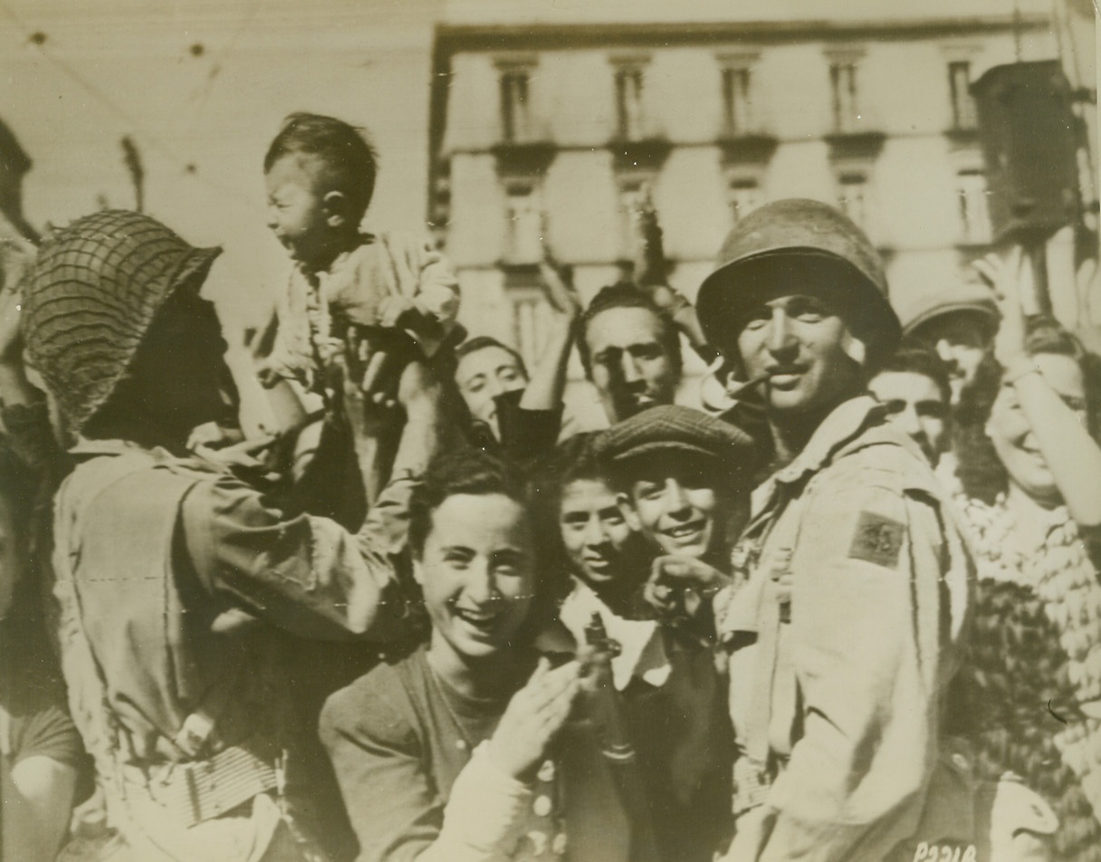 Yanks Welcomed in Naples, 10/4/1943. Natives of Naples smile as they welcome American soldiers to that city. One soldier (left), holds a baby, who doesn’t seem to share the happiness of the hour. This photo was flashed to the U.S. by Radiotelephoto. Credit Line (ACME Photo via U.S. Army Signal Corps Radiotelephoto);