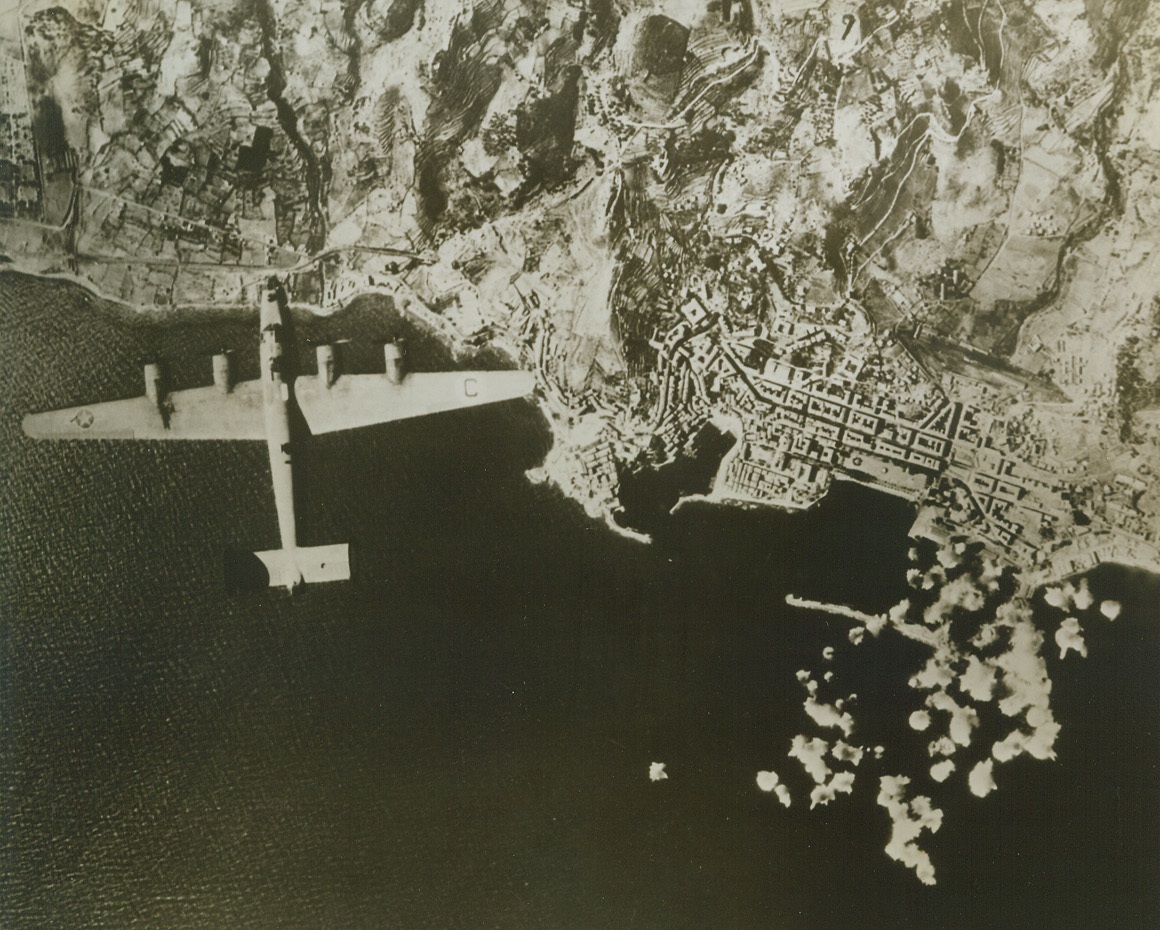 LIBERATORS BOMB CORSICA, 10/22/1943. BASTIA, CORSICA—More than fifty bomb bursts may be seen in the upper left harbor and on dock facilities at Bastia, as Liberators of the U.S. Army Air Forces raid the Corsican port. Hits were made on a large merchant vessel, three small merchant ships, and in the railroad yards. This remarkably clear photo shows the methods of contour farming that are practiced in many parts of the Mediterranean. Credit: U.S. Army Air Forces photo from Acme;