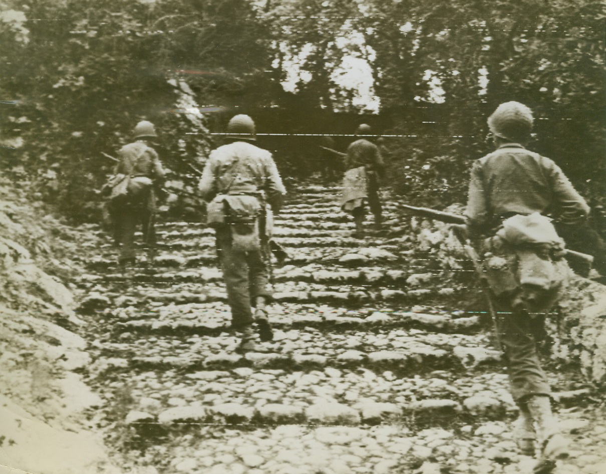 AFTER THE GERMANS, 10/20/1943. CAIZZO, ITALY—An American infantry patrol, their guns held ready, advances double time up a flight of steps in the outskirts of Caizzo, in pursuit of fleeing German troops. Today, Nazi forces are retreating to a new mountain line along Massico Ridge, after shooting civilians and burning farms in the Volturno Valley. This photo was flashed to the United States today. Credit: U.S. Signal Corps radiotelephoto from Acme;