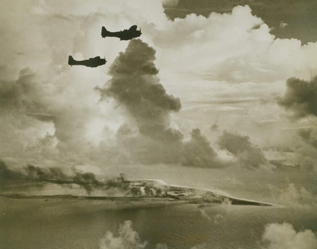 REVENGE AT WAKE, 10/25/1943. WAKE ISLAND—Two Douglas Dauntless dive bombers roar over Wake Island before wheeling down to drop their bombs, October 6, when a U.S. carrier task force destroyed 61 Jap planes, many ships, barracks and other installations. Before the day ended, the enemy island base was a shambles. Credit: U.S. Navy photo from Acme;