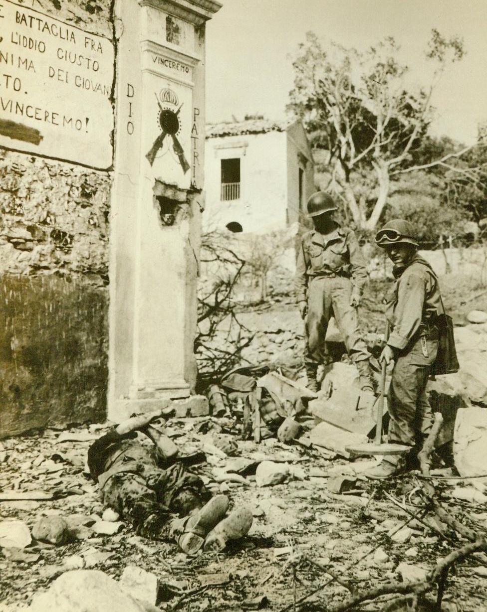 American Victim of Nazi Booby-Trap, 10/4/1943. This American soldier, (left, foreground), killed by a Nazi booby-trap in Sicily, fell before a sign extolling Fascism and ending with the word “Vincermo”, whichmeans “We will Win”. Before the Yank’s buddies could approach his body, they had to use a mine detector to make sure there were no more Nazi traps.  10/4/43 (ACME);