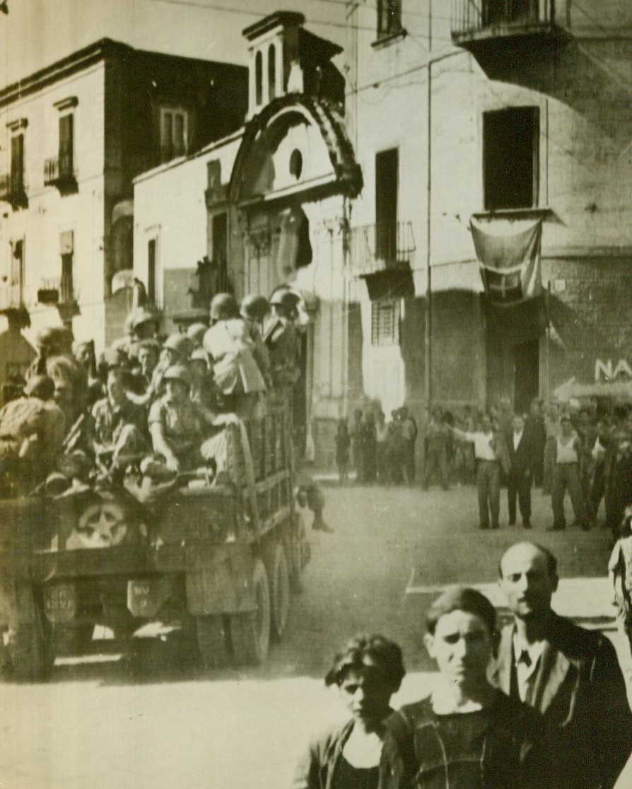 American Troops Enter Naples, 10/4/1943. In this photo flashed to the U.S. today by Radiotelephoto, a truck loaded with U.S. troops rolls into Naples, Italy, as natives stand by to watch them. Note arrow, (right, background) indicating the route to Naples Proper. 10/4/43 (ACME);
