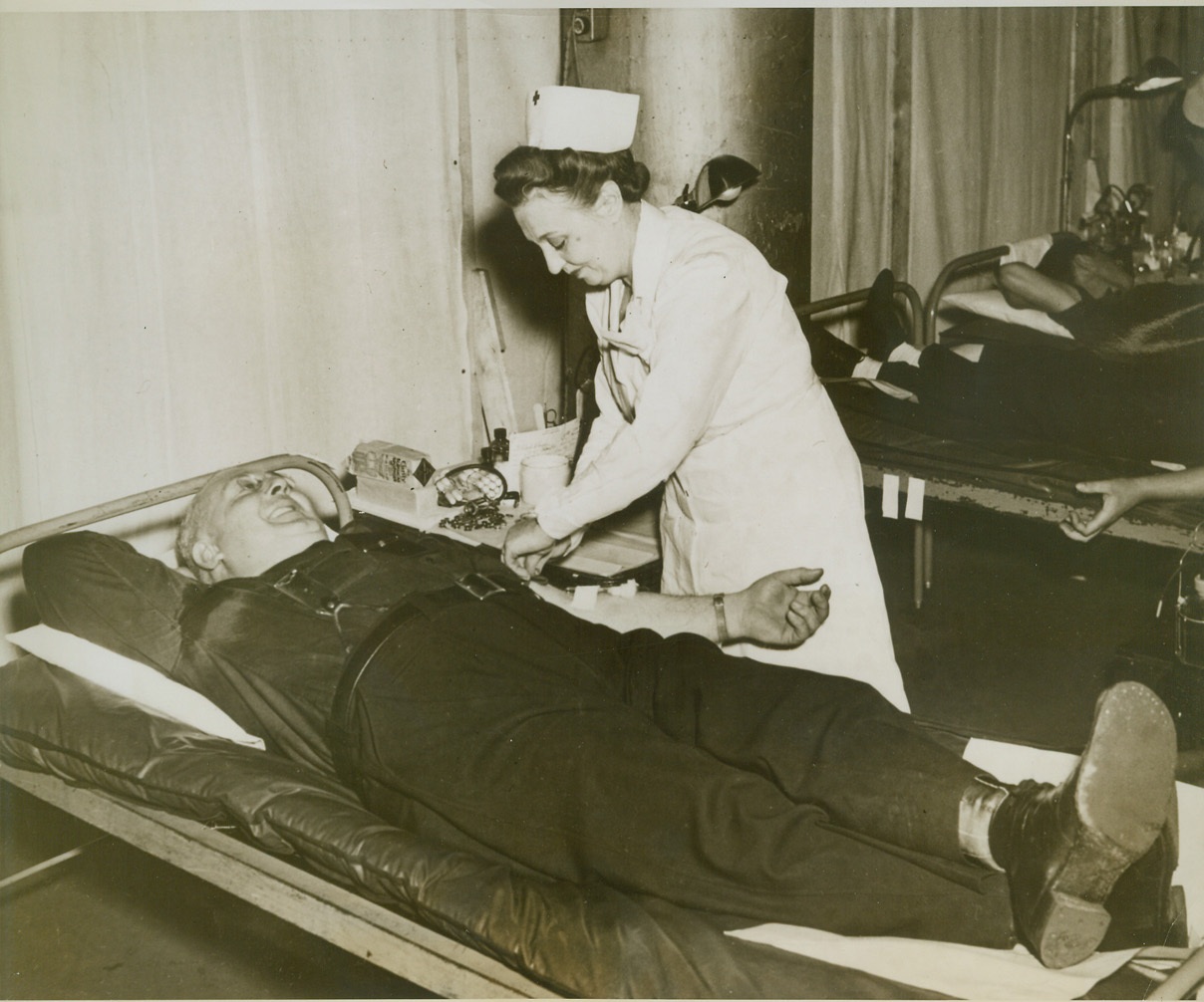 REUNION AT A BLOOD BANK, 11/10/1943. DETROIT, MICH. – When Karl Miller came to the Red Cross Blood Bank Mobile Unit to give his donation he found Nurse Freida Schaub in attendance. The two had worked at the same base hospital in Scouilly, France, during the First World War. They are shown in the Mobile Unit as it stopped at the Hudson Motor Car Co. Detroit Plant. Credit: ACME;