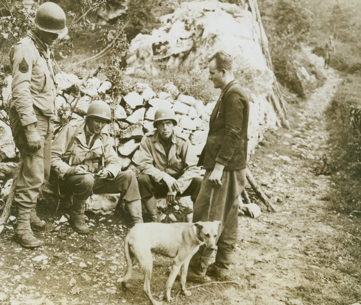 Canine Causes Capture of Master, 11/20/1943. ITALY – Sgt. Roy Biekn, of Klemath Falls, Ore., attached to Prisoner of War section of the Military Police; Capt. Richard A. Smith, and Lieut. Roy Moore, of Fargo, N.D., (left to right), cross-examine a German prisoner, garbed in civilian dress, who was captured by Captain Smith when he overheard the prisoner give orders to the dog in German. The dog was used for messenger services by German troops. The three Americans are attached to an Infantry regiment.  Credit Line (U.S. Army Official Photo from Acme);