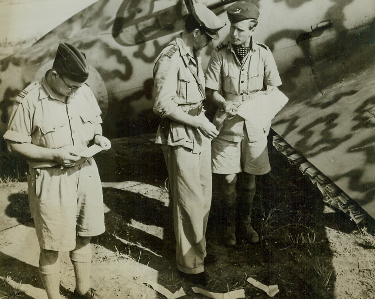 We “Bomb” Rome With Leaflet, 11/5/1943. ITALY—Leaflets are neatly packed between the wing and flaps of this Italian plane which will bombard Rome with messages. R.A.F. officers discuss the route at a recently captured airport. The pilot will lower the flaps over the “Target” area. Credit: ACME.;