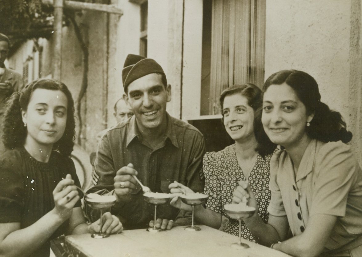 Yank Meets His (Foreign) Country Cousins, 11/17/1943. PALERMO, SICILY—It isn’t every Yank who can go overseas and find three pretty relatives to make him feel at home in a foreign country. Lucky Sgt. Vincent J. Crivello of Milwaukee, Wisc., was mighty pleased when he discovered his comely cousins in Palermo. He was the envy of his buddies when he took the girls out to a sidewalk café for some good ole American sundaes. Credit: OFFICIAL OWI PHOTO FROM ACME.;
