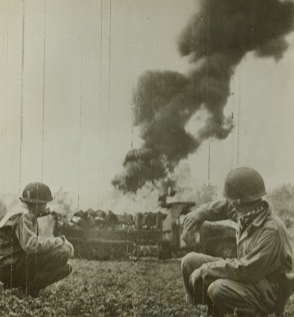 GERMAN BULLS-EYE ON GASOLINE CARRIER, 11/11/1943. Gasoline carrier truck of the U. S. Fifth Army blazes after being hit dead-center by German strafing planes, in the central sector front in Italy. American officers in the foreground shield their faces from the intense heat of the flames as they watch the progress of the blaze.Credit: Acme photo by Bert Brandt for the War Picture Pool via Signal Corps Radiotelephoto;