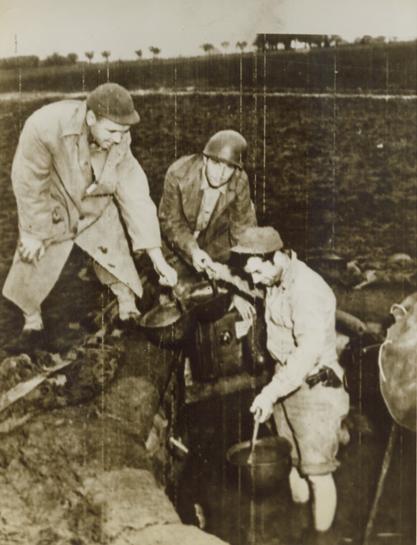 BAILING OUT, 11/26/1943. ITALY—Forming a helmet brigade, members of an anti-aircraft crew bail out more than 18 inches of water that gathered in their gun emplacement as torrents of rain descended upon them in Italy. Left to right: Pfc. Woodrow Porter, of Dover, Tenn.; Pfc. Edward J. Zvonek of Detroit, Mich.; and Pvt. George Cooper (in pit) of New Bedford, Mass.Credit: U.S. Marine Corps photo from Acme;