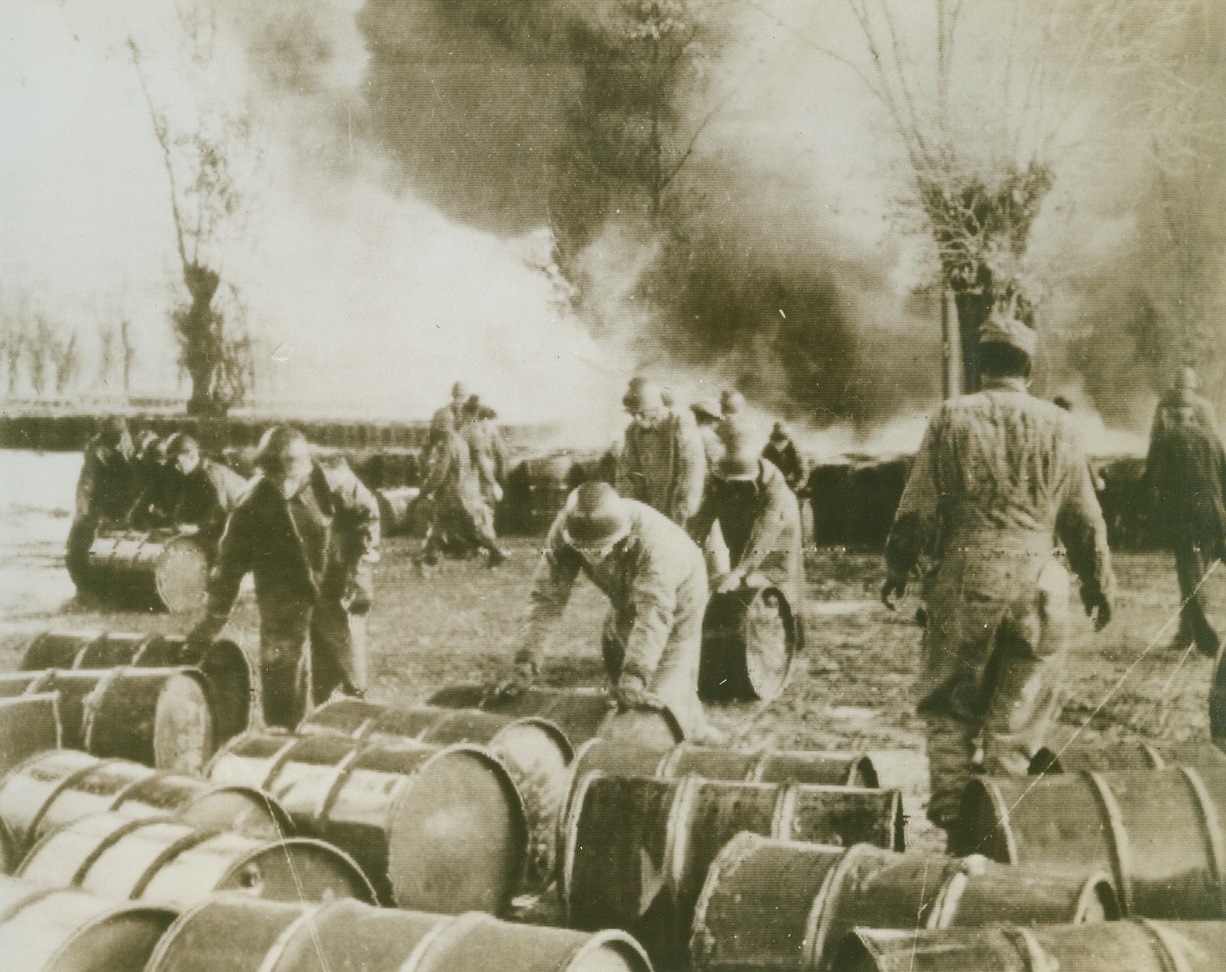 ONE FOR THE NAZIS, 11/26/1943. ITALY—American Fifth Army troops work frantically to save barrels of gas and oil from flaming destruction, after the Germans scored a hit on al Allied fuel dump near Aversa, Italy. Flames in the background are a source of danger to both the workers and the precious fuel they roll to safety. Credit: Acme Radiophoto;