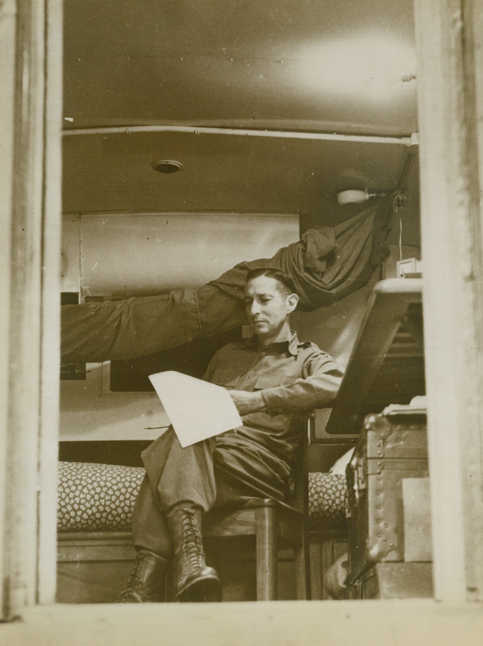 THE GENERAL, AT EASE, 11/10/1943. ITALY—Seen through the open door of his trailer, in which he lives throughout the campaign, Lt. General Mark W. Clark relaxes alongside his cot as he reads an official report. Credit: Acme;