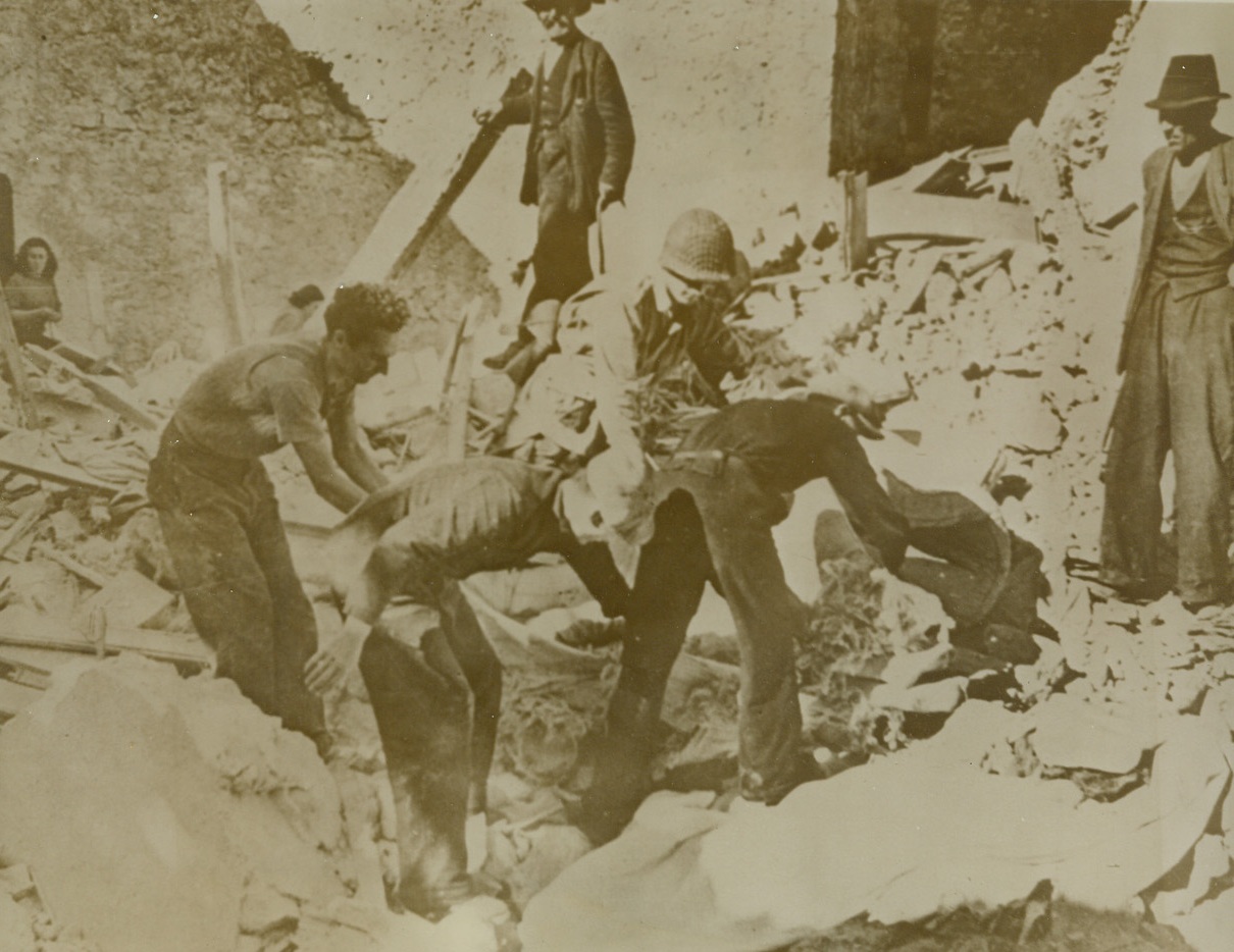 Grim Job, 11/24/1943. PRATA, ITALY – To those who lived after the fleeing Germans blew up a road block in Prata, fell the grim job of removing the bodies of those killed in the explosion from the wreckage. Pvt. Dick Heusle of Mexia, Texas, helps Italian civilians remove the body of a young woman from the ruins. Credit Line (ACME);