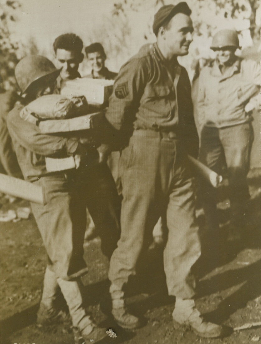 Santa Was Good to Him, 11/27/1943. SOMEWHERE IN ITALY -- Lucky Pvt. Charles "Snuffy" Schmitz, of New York City, hit the jackpot, so far as Christmas gifts from home were concerned. The doughboy collected so many packages from home that he needed help to get them to his tent. T/4 John W. Griffin of Western Springs, Ill., thinking of the chocolate cake and toll house cookies that might be hidden beneath those paper wrappings decided to lend a helping hand. Credit (Signal Corps Radiotelephoto from ACME);