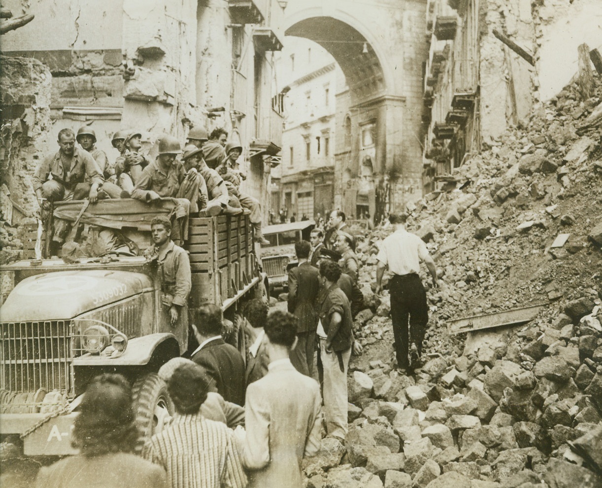 Returning Naples to Normalcy, 11/2/1943. NAPLES, ITALY – A group of 5th Army Unites States troops are held up in Naples as a labor group clears away debris of bomb wreckage from the streets of the city. Credit (PWB Photo from OWI via Acme);