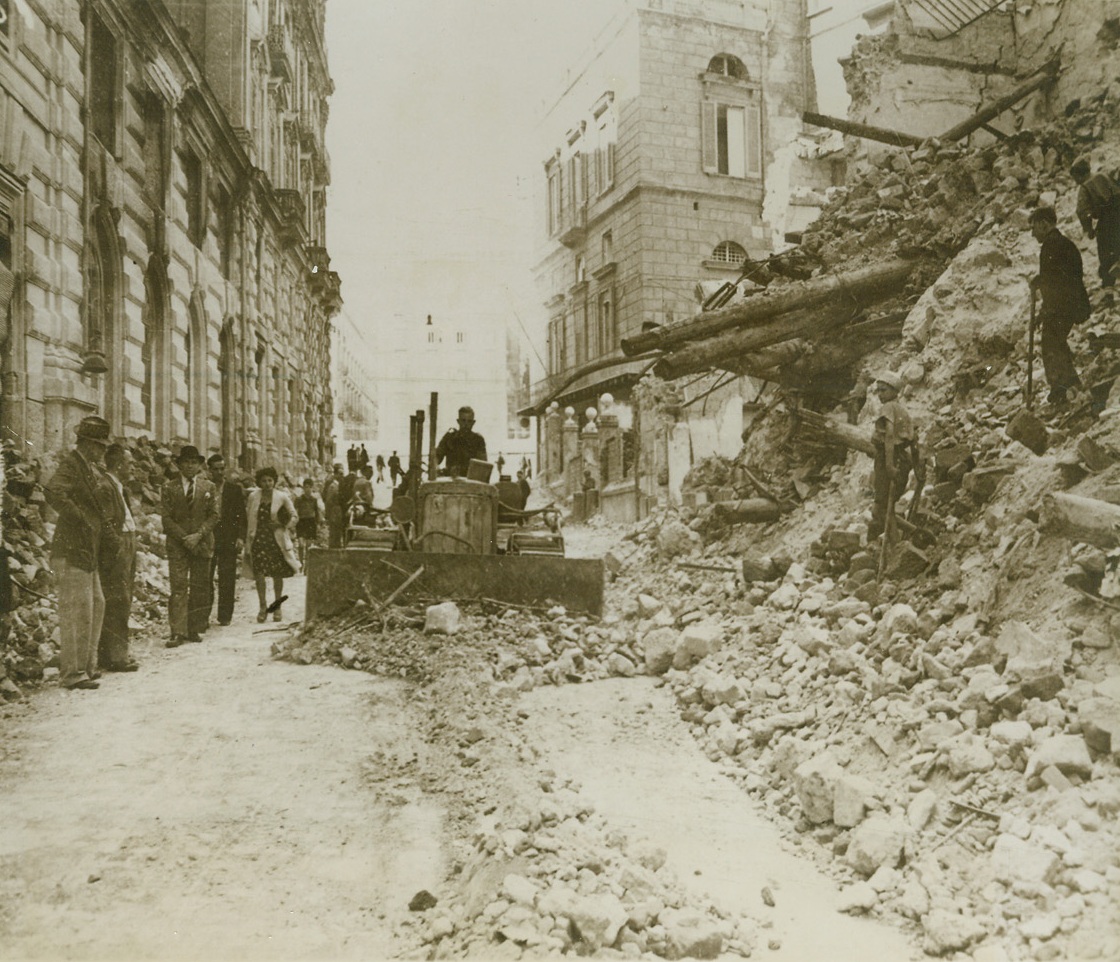 Returning Naples to Normalcy, 11/2/1943. NAPLES, ITALY – A bulldozer scrapes the debris from the streets of Naples as citizens looks on. The rubble silently testifies to the havoc wrought by war. Credit (PWB Photo from OWI via Acme);