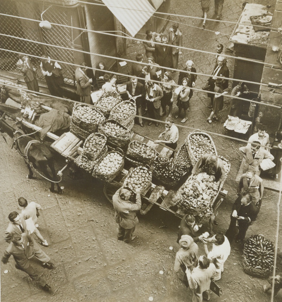 NEAPOLITAN PRODUCE MARKET SCENE, 11/2/1943. Shortly after Allied forces entered Naples, AMG encouraged natives to bring all kinds of vegetables and fruits from nearby villages. All available transportation, from hand-pushed carts to old, broken-down trucks hauled produce and helped relieve immediate food shortage, while bread was still not available. A maximum price was established on everything to avoid black market. Carts traveled most populated streets and were sold out immediately, necessitating two or three trips a day. Credit: Acme;