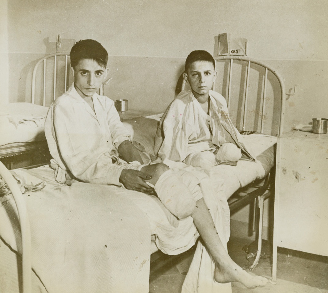 VICTIMS OF NAZI “SPORT”, 11/4/1943. NAPLES, ITALY—These two Italian lads, Guido Brandi, 13, and his brother Thomaso, 16, (left), were working in a field near the city during the German occupation of Naples. Two German soldiers appeared in the window of a nearby window and beckoned to the boys, who drew near hoping for a bit of food, or a present. They got the present, all right—a grenade was tossed at them by one of the Nazis. The lads tries to catch it. One lost both legs, the other one leg. They are shown, here, recovering in a Naples hospital. Credit: Acme;