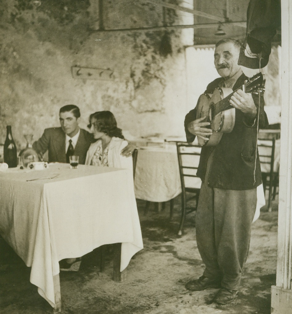 TROUBADOR REVIVES SPIRIT OF NAPLES, 11/2/1943. Recently released photo shows the resurgent spirit of Neapolitans, who, despite shortage of restaurants there, maintain the old romantic spirit. Shown here is an old ballad singer, a reminder of the former gay old tourism times, entertaining sweethearts as they wait for their meal of black spaghetti; a little fish and good, coarse red wine. Credit: Acme;