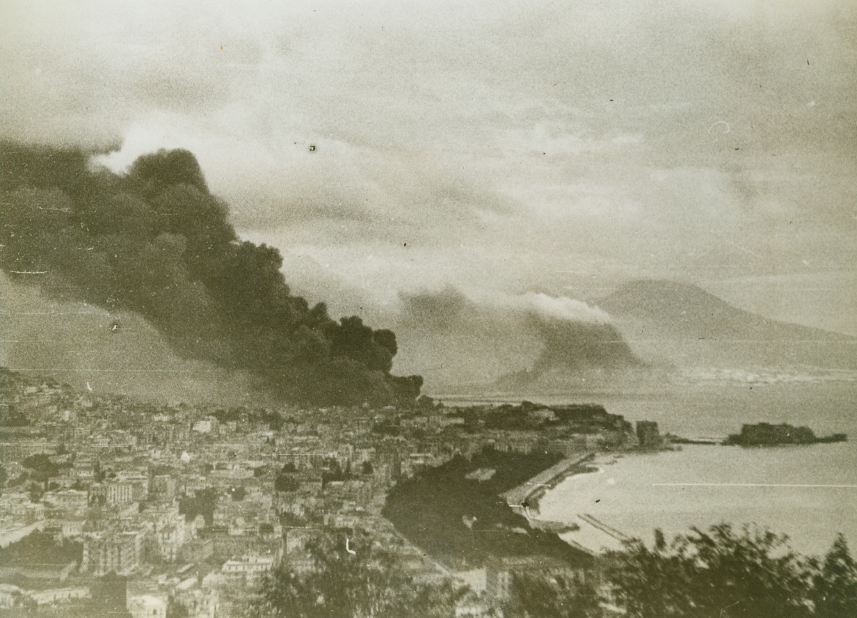 NAPLES FIGHTS NAZI TERRORISM, 11/2/1943. This series of photos, just released in the United States, tells the graphic story of the German rape and pillage of Naples, how they killed Neapolitans just because they were Italians, and how Nazi demolition squads razed buildings and beautiful landmarks of no military value—but to create another blackened and twisted monument to German terrorism and vengeance. But Naples fought back and many young Italians—some only 14 years old—brought out firearms that they had kept hidden and, for three days before the Allies captured the city, kept up guerilla battles against the Germans. These young lads, who were members of an anti-Fascist organization led by one Antonio Tarsia, killed as many as 30 Germans each day by ambushing them and sniping from rooftops. The fighting, however, was one-sided in the face of the superior numbers of the Germans. About 2,000 citizens of Naples were shot down in the streets or in their homes just because they happened to be Italians.  NEW YORK BUREAU Smoke begins to cover Naples as the Nazis worked with terrible fervor to destroy buildings and installations in the face of the advancing Allied 5th Army. Credit: Acm;