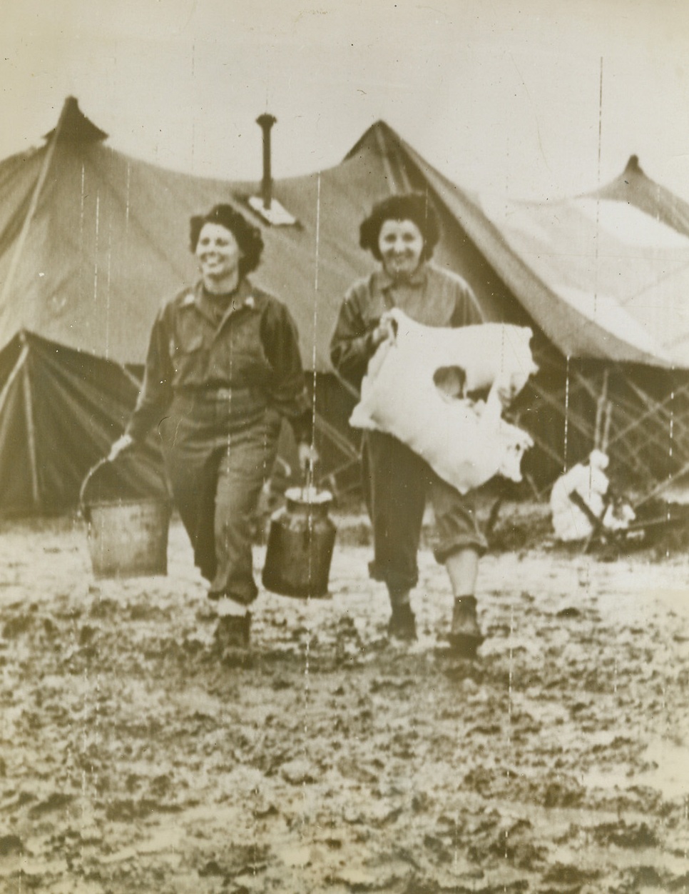 ONCE CALLED “WOMEN IN WHITE”, 11/22/1943. ITALY—A pair of Army nurses slog cheerfully through a sea of mud in Italy, where continuous rains have bogged down both Allied and Nazi ground attack. They are (left to right) Lt. Sylvia Hamper, Joliet, Ill., who carries pails used for mixing plaster, and Lt. Anna Lange, of Ashley, Ill., who holds a section of a prefabricated plaster cast. Credit: Acme photo by Bert Brandt, for the War Picture Pool via Army radiotelephoto;