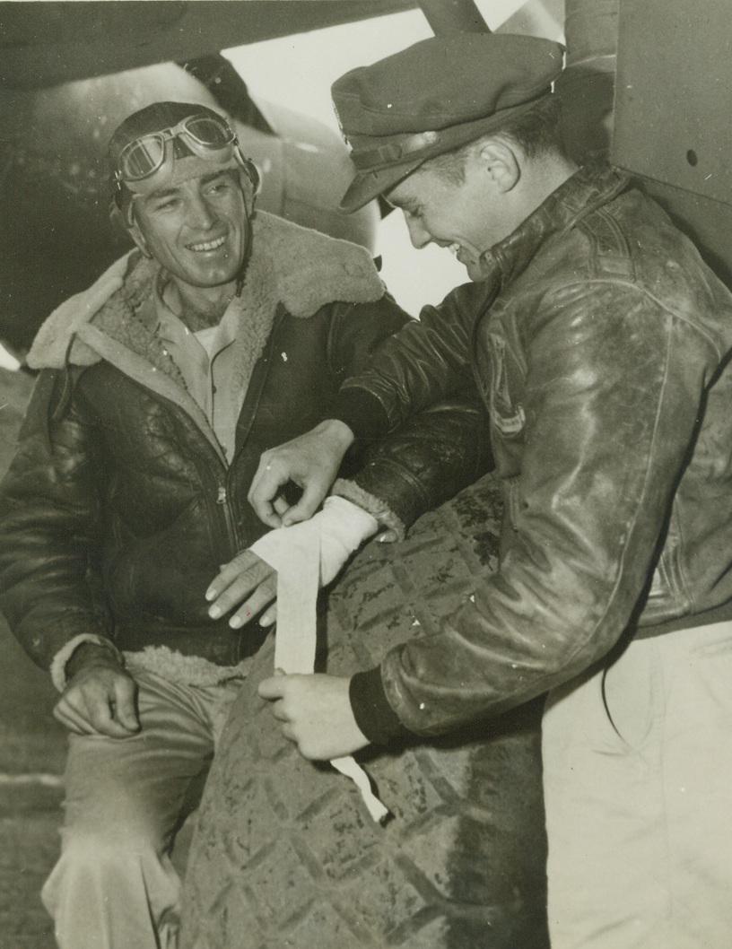 TOP BOMBER GUNNER GETS 7 JAPS IN ONE SCRAP, 11/1/1943. CHINA—T/Sgt. Arthur Benko, Bisbee Arizona, has cause to grin, even though he has a slight hand wound being bandaged by Capt. James Maher, adjutant of the heavy bomber group in China. Benko, member of the group, shot down seven Jap Zeros in one fight, bringing his score to 16 confirmed Zeros downed. This makes him leading bomber gunner of the China, India, Burma Theatre—and perhaps in the world. Credit: Acme;