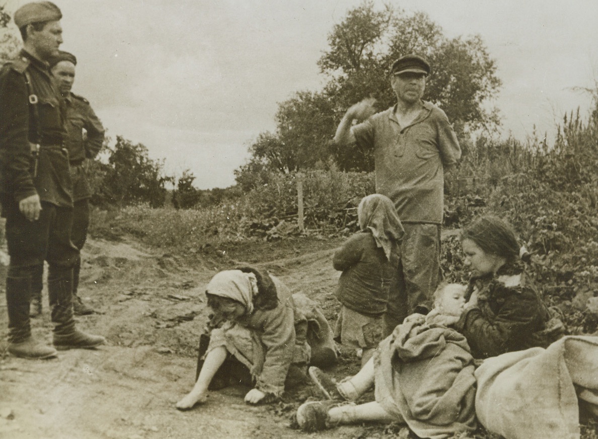 After Germans Despoiled Their Farm, Orel, Russia – Two Red soldiers, listen sympathetically as Ivan Merkulov, (standing at right), a worker on the Volkovo State Farm in the Orel Region, tells how the farm was plundered, and how his family, (at his feet), were harried by the Germans before they were forced into retreat in the region by Soviet forces. Her face mirroring sadness as she listens to the story, the farmer’s wife, (right), nurses her baby. (Passed by Censors).Credit: ACME;