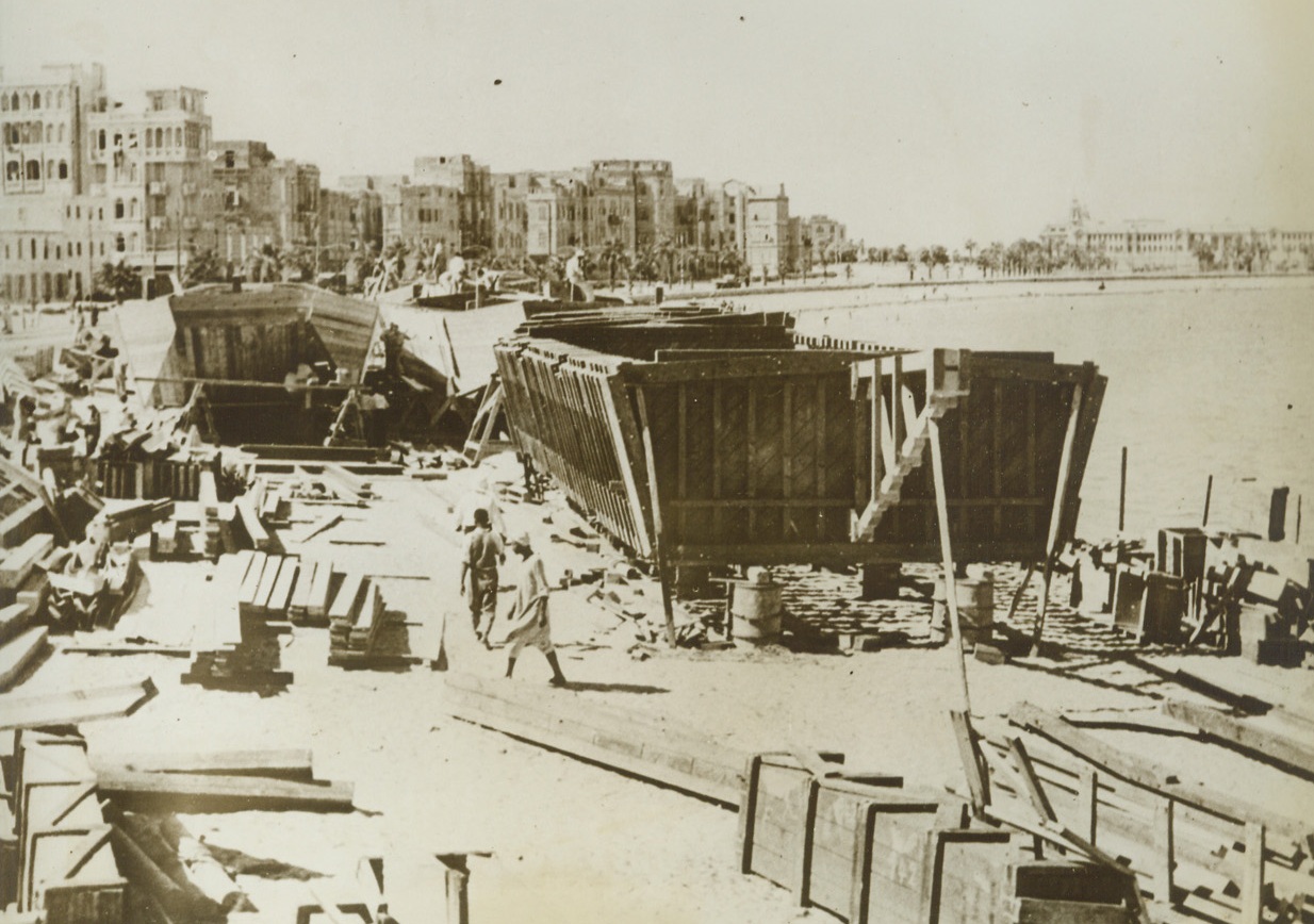 Wood and Canvas Barges to Carry 200 tons, 11/1/1943. Alexandria, Egypt – With materials sent from America, local labor at Alexandria fashions a new type of naval lighter, constructed entirely of wood and canvas.  The flat-bottomed barge will carry 200 tons of cargo. Credit line (ACME);
