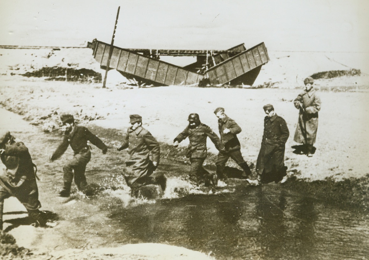 On the Double, 11/21/1943. Somewhere in Russia—A single Red Army man is all that’s needed to keep these captured Nazis hopping. Captured on the Russian front, the Germans dash past a damaged railway bridge and through a stream to join their comrades at a nearby prison camp. Their lines cracking and their spirit failing in the face of the Soviet offensive, thousands of Nazis are abandoning their arms, tanks and guns and going into captivity.  Credit: ACME.;