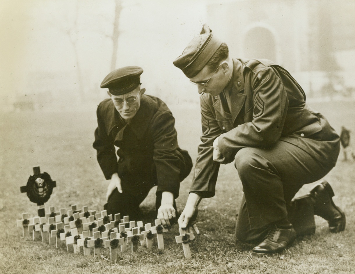 TRIBUTE TO THE FALLEN, 11/15/1943. LONDON, ENG.—Many American servicemen have placed crosses in the American section of the Field of Remembrance on the lawns outside Westminster Abbey, to pay tribute to the memory of their comrades who have been killed. Here, First Class Electrician Leo Barron, (left), USN, of Arkansas, Texas; and Sgt. W.H. Donnelly, of Flushing, N.Y., place miniature crosses in the Field of Remembrance. Credit Line (ACME);