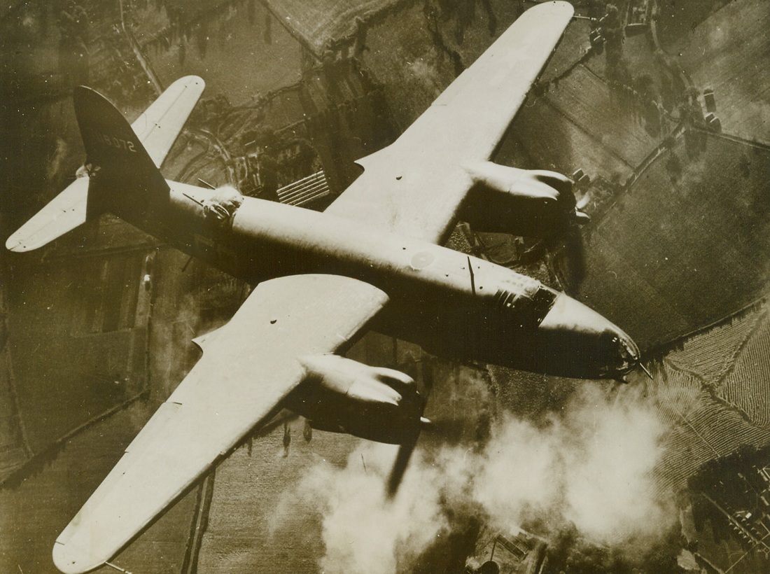 BOMBS HOME OF “YELLOW NOSES”, 11/26/1943. TRIQUEVILLE, FRANCE—Like a huge, angry bird of prey, a Martin B-26 Marauder soars over the Nazi fighter base at Triqueville, France, the home of some of Goerings’ famed “Yellow Nosed” fighter planes. Stick after stick of 300-pound bombs drop from the medium bomber and its fellow raiders, blasting hangars, buildings and dispersal areas of the airfield. Credit (U.S. Army Air Forces Photo from ACME);