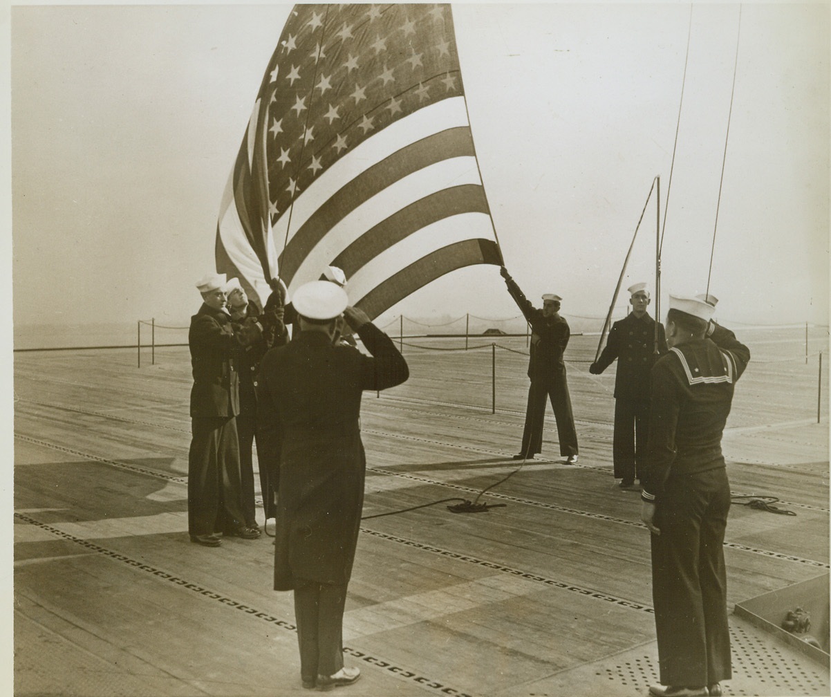 New Aircraft Carrier Honors Bataan, 11/17/1943. Philadelphia, PA.—A new carrier, named in honor of the heroes of Bataan was commissioned at the Philadelphia Navy Yard today. Ship’s officer and men raise the colors. Credit: ACME.;