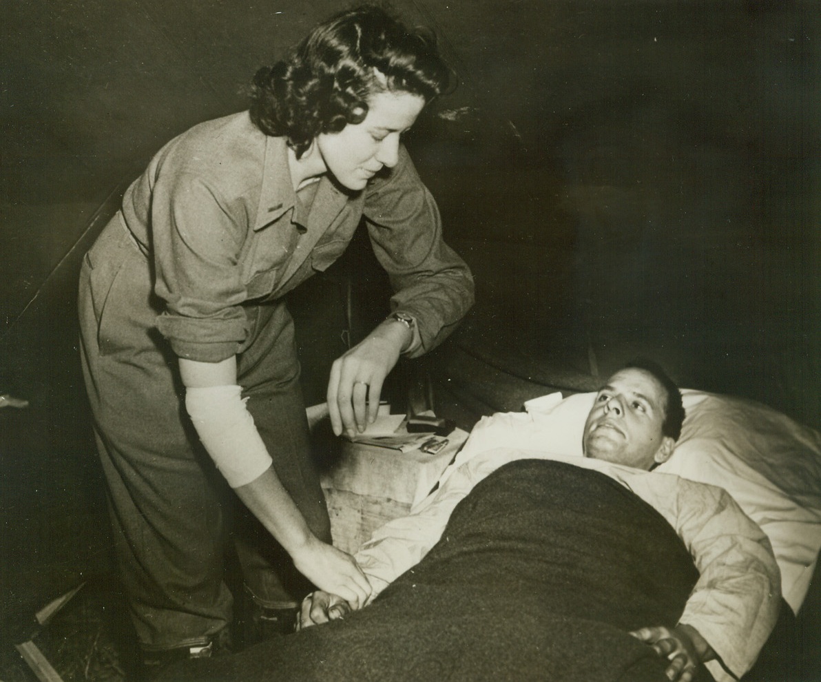 WOUNDED NURSE CARRIES ON, 12/29/1943. AT A FIELD HOSPITAL SOMEWHERE IN ITALY—Lt. Cordelia E. Cooks, first Army nurse in Italy to be wounded by enemy fire, sustaining a shrapnel wound, refuses to take time out to recover. With her arm bandaged she attends a patient, Pfc. Joseph Uhrin, Latrobe, Pa., member of a field artillery unit on the day after she received her wound. Lt. Cooks is from Ft. Thomas, Kentucky.Credit: Signal Corps photo from Acme;
