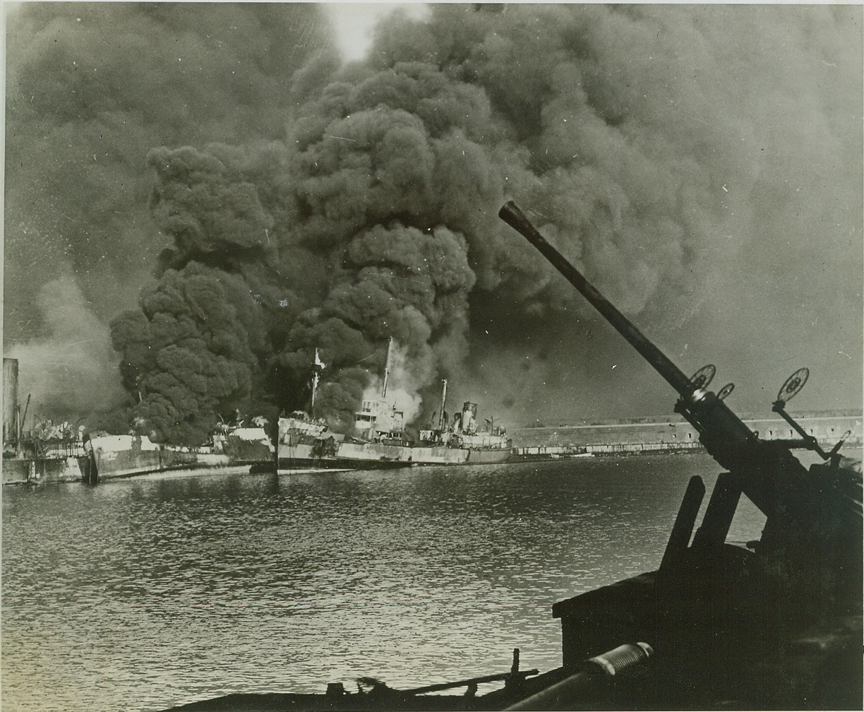 Axis Attack on Bari, 12/16/1943. In the shadow of an anti-aircraft gun, Allied ships burn furiously in the Southern Italian port of Bari, following a German air raid on Dec. 2, 1943. Secretary of War Stimson today announced that two ammunitions ships were hit and the resultant explosion caused spreading fires which destroyed or damaged a number of Allied cargo ships and small harbor craft. There were an estimated 1,000 casualties, including 37 American naval personnel. Credit Army Signal Corps Photo From (ACME);