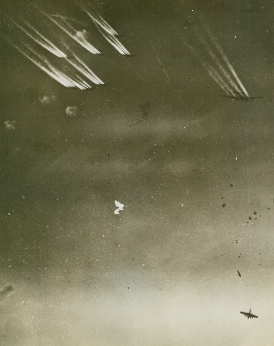 Carry On, Mates, 12/28/1943. A U.S. flying fortress (lower right) is brought to earth, its tail piece following, as other of the giant planes continue to unleash bombs over Bremen, Germany. The 8th Army Air Force bombers leave their contrails in the flak filled sky, where more devastation goes hurtling downward than is tossed up from Nazi guns. Credit: U.S. Army Air Force photo from ACME.;