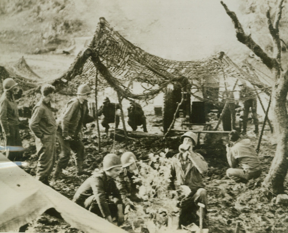 Christmas at the Front, 12/29/1943. Italy—Between rounds in the hills above San Vittore, this American gun crew with the Fifth Army snatches a moment to celebrate Christmas. Clustered around a tiny tree set up behind their barking cannon, the boys drink a toast from their canteens and exchange good wishes. Credit: U.S. Signal Corps radiotelephoto-ACME.;