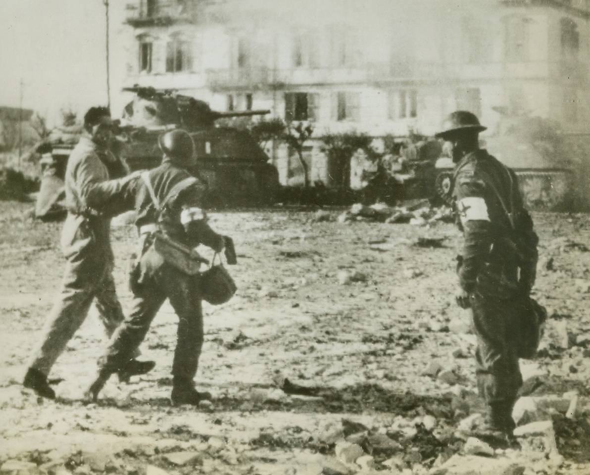 Assisting Wounded Commander, 12/31/1943. Ortona, Italy—A tank commander, who was shot when he opened a turret to check firing results, is led to a dressing station by a medical attendant. The two men walk through the littered streets of battleworn Ortona, which fell to troops of the British Eighth Army after eight days of fighting. Credit: OWI radiophoto from ACME.;