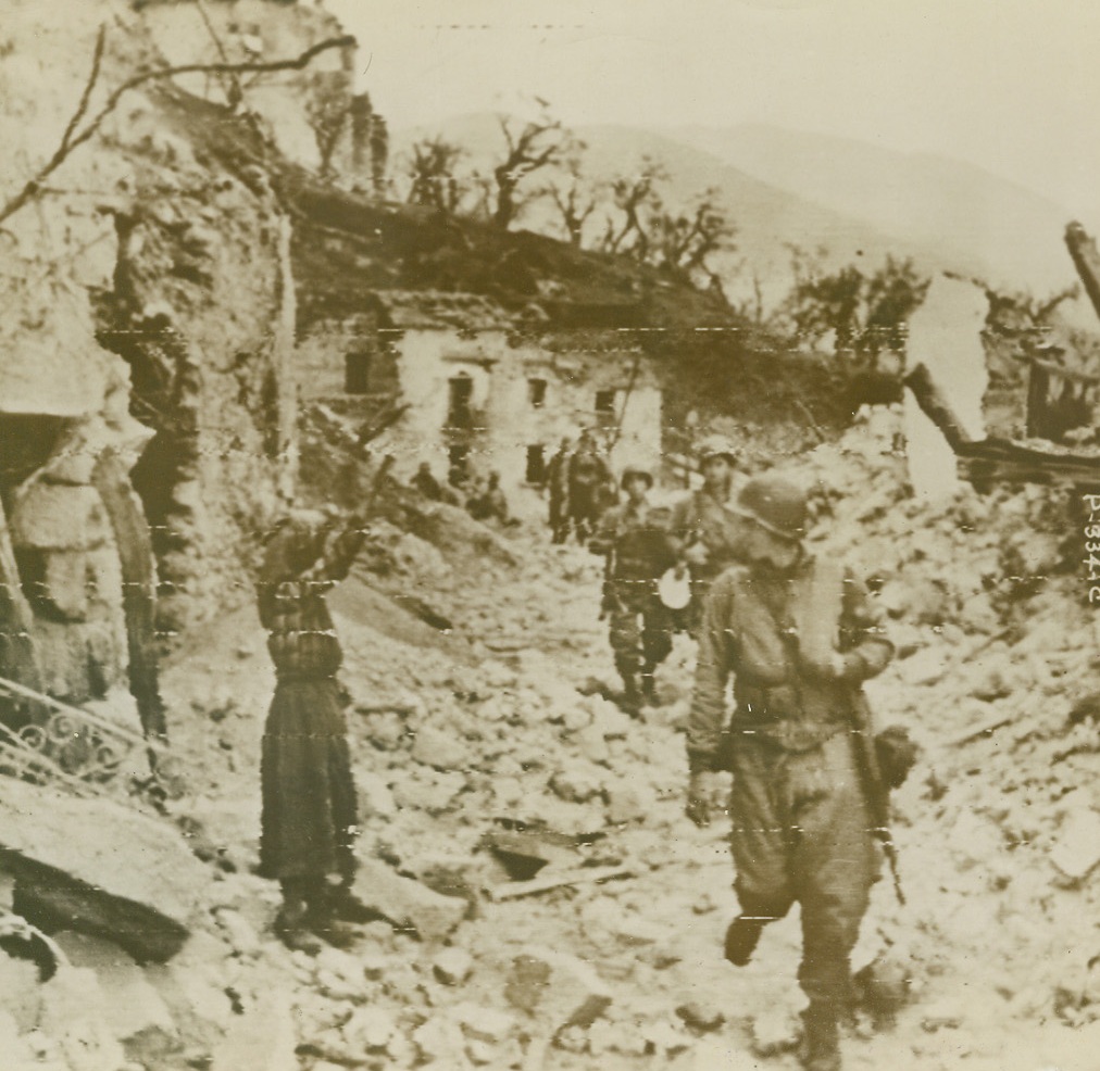 HAIL THE CONQUERORS!!!, 12/21/1943. SAN PIETRO, ITALY—Advancing Yanks receive first greeting from a native woman standing amid a debris-covered street outside her cellar shelter as they enter San Pietro. Credit: Signal Corps radiotelephoto from Acme;