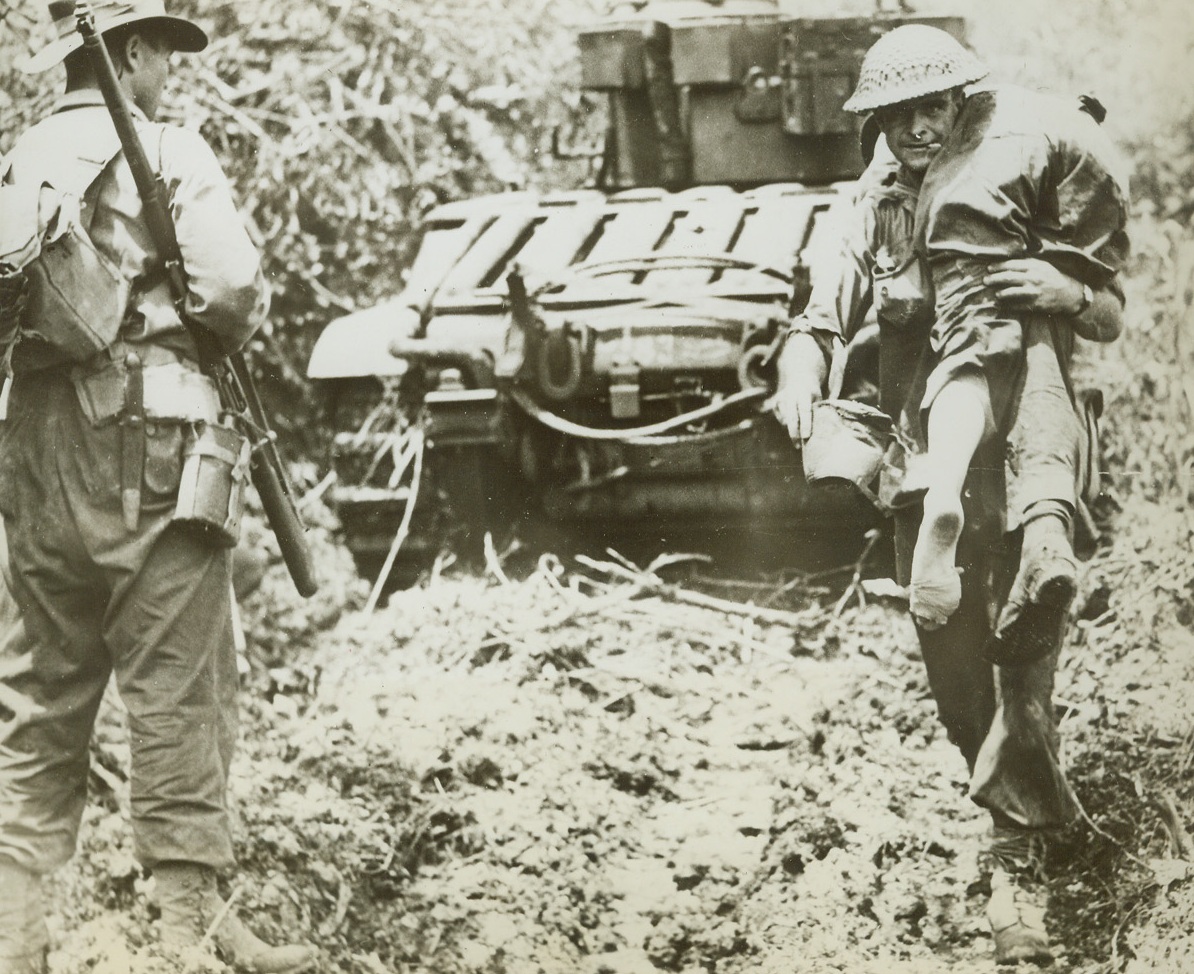 Wounded Aussie Comes Back, 12/29/1943. Satelberg, New Guinea – Slung over the shoulder of one of his buddies, a wounded Australian fighting man is carried back from the front lines. The rescuer passes a tank that continues in the attack on Satelberg. Credit: ACME;